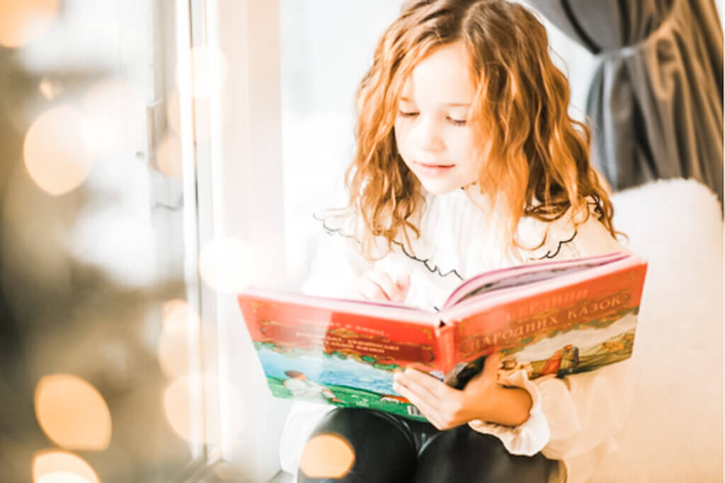 Image of young girl on her bed reading what appears to be a Christmas book - concept of beautiful Christmas picture books