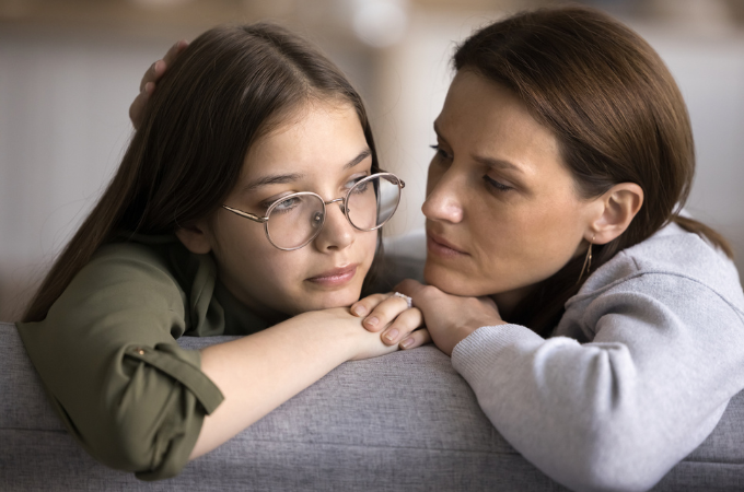 image of mother and teenager daughter sitting on the sofa; teen is upset and mom is holding space for the girl to be sad