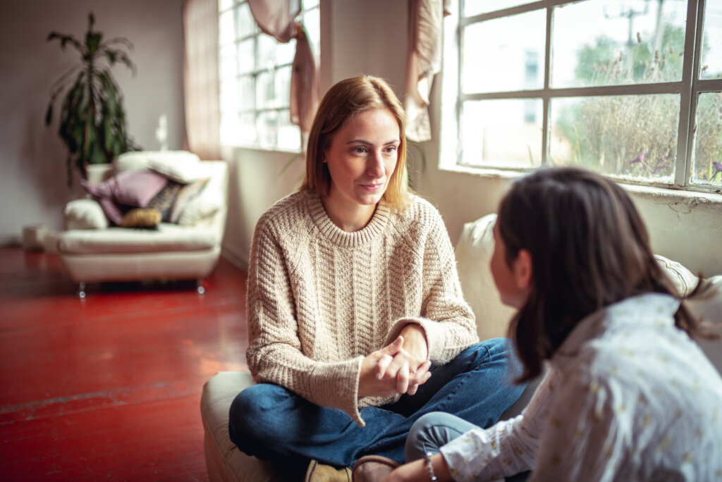 An image of a mother and teen daughter talking at home on the sofa. Mom is intently listening to daughter talk. Concept of: If you're wondering how to validate someone's feelings - it starts with listening attentively. Not as you formulate your responses - but as a way to really understand how the other person is feeling.